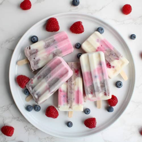 Healthy 4th of July Popsicles pops on a plate with berries