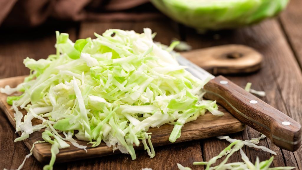 shredded cabbage on top of a wooden cutting board with a knife