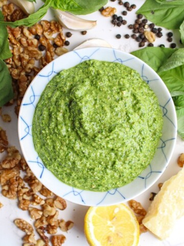 pesto without pine nuts in a small bowl surrounded by herbs and walnuts