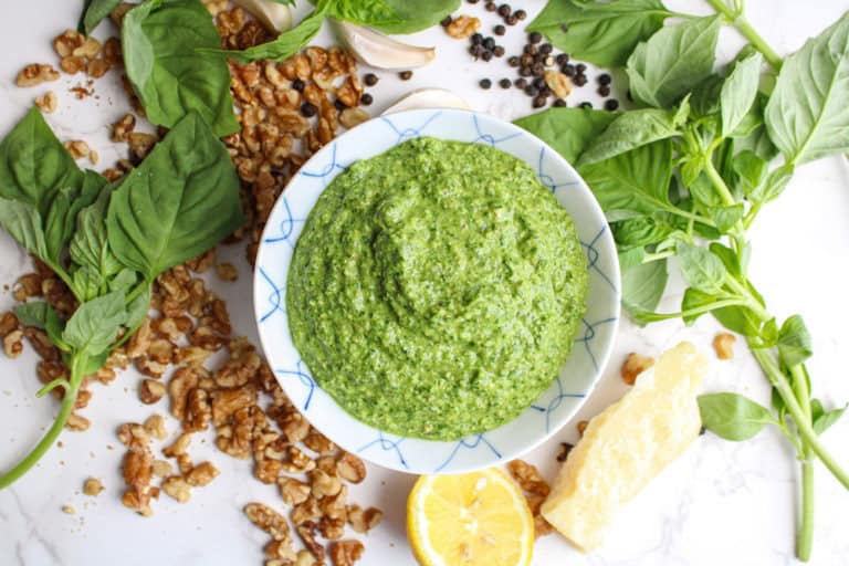 pesto without pine nuts in a small bowl surrounded by herbs and walnuts