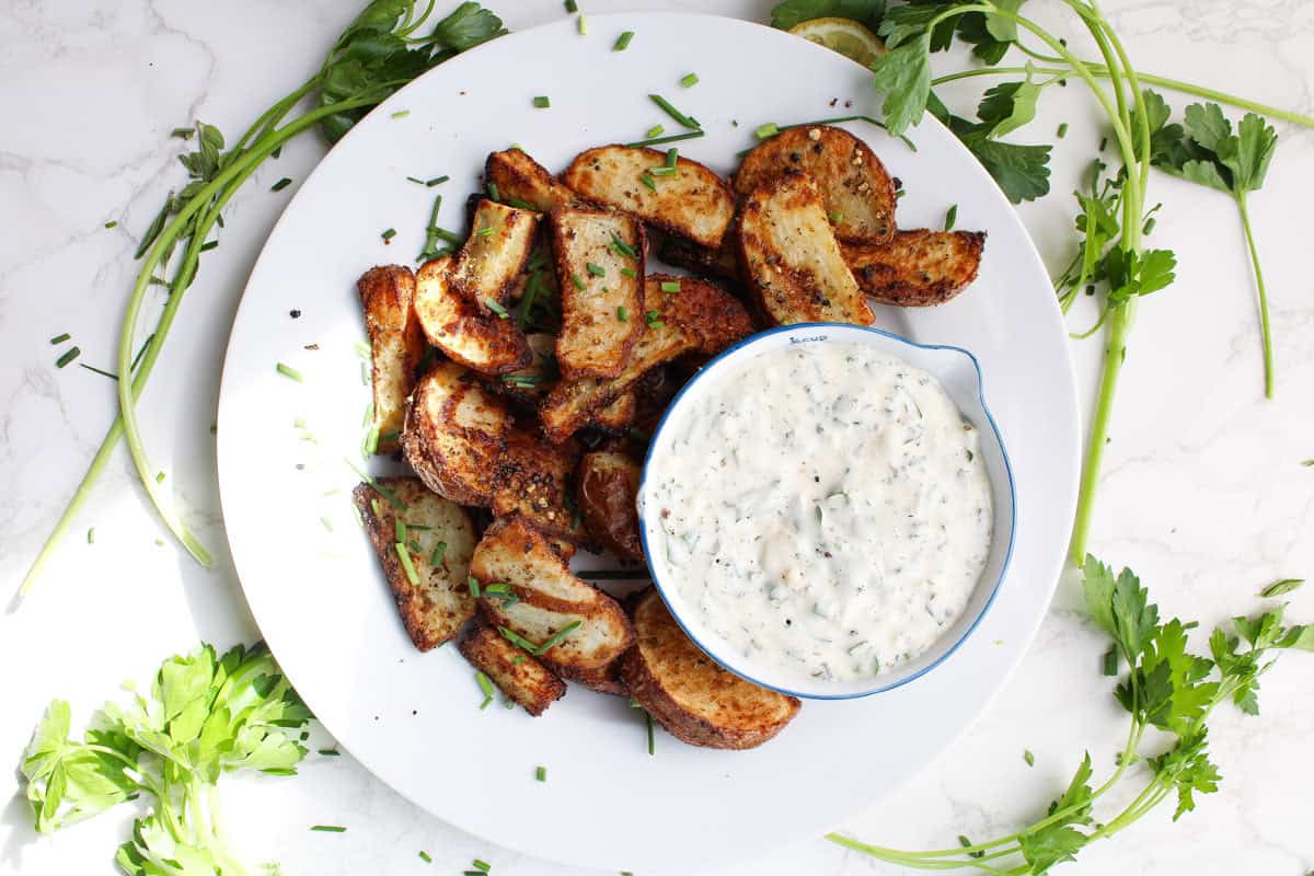 air fryer red potatoes plated with cream dip and fresh herbs around white plate