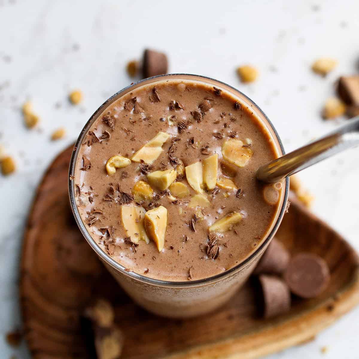 peanut butter chocolate smoothie in a glass with straw garnished with peanuts and chocolate shavings
