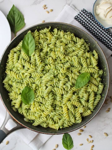 Ricotta pesto pasta in a large frying pan garnished with fresh basil